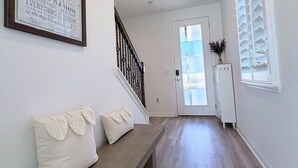Un couloir avec un banc, une citation encadrée au mur et une porte avec des stores.