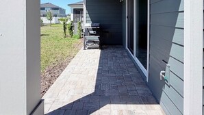 Un patio couvert équipé d’un barbecue et de mobilier d’extérieur, donnant accès à une porte-fenêtre coulissante.