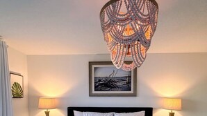 Un lit bien fait, avec une literie blanche, deux tables de chevet avec des lampes, un tableau encadré au mur et un lustre original.