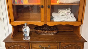 A wooden cabinet with glass doors, containing books, towels, and a bottle of hand sanitizer.
