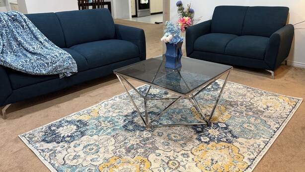 A living room with two dark blue sofas, a glass coffee table, and a patterned rug.