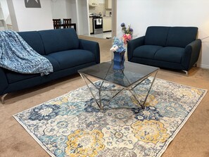 A living room with two dark blue sofas, a glass coffee table, and a patterned rug. - Spacious basement apartment in Georgetown, GTA (Halton Hills)