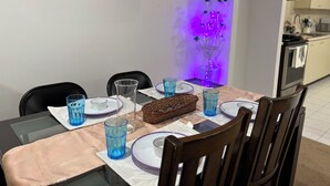 A dining area with a table set for four, chairs, a vase, and a wall clock.