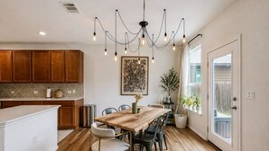 Een keuken met houten kastjes, een eettafel met stoelen, een kroonluchter en een potplant.