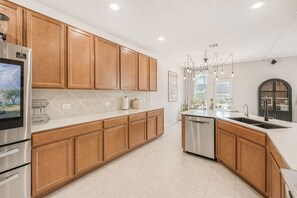A modern kitchen with wooden cabinets, stainless steel appliances, and a large island with a sink. - NEW Stylish 3BR by Tesla, Airport + F1 (Del valle)