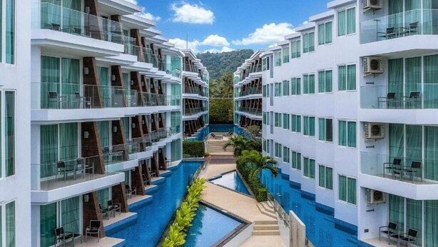 A modern hotel with a central swimming pool, multiple balconies, and a mountain backdrop.