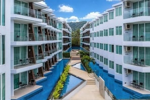 Ein modernes Hotel mit einem zentral gelegenen Schwimmbad, mehreren Balkonen und einem Blick auf die Berge.