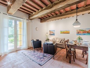 A spacious living room with a wooden ceiling, a dining area with a table set for two, and a large window with curtains. - Apartment in Tuscany With Stunning Views (Capannori)