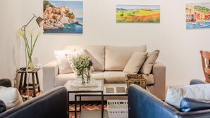 Ein Wohnzimmer mit einer Couch, Sesseln, einem Couchtisch und Wandbildern, die Küstenlandschaften zeigen.