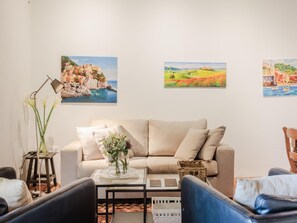 A living room with a sofa, chairs, a coffee table, and wall art depicting coastal scenes. - Apartment in Tuscany With Stunning Views (Capannori)