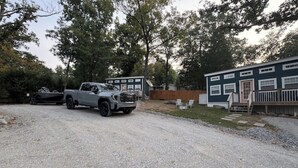 A gravel driveway leading to a building with a wooden deck and a truck parked nearby. - Freedom-Cabin-1 @ Eagle Hollow (Goreville)