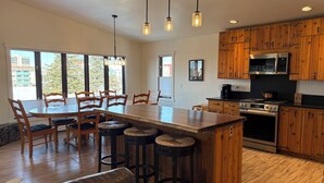 Una cocina moderna con armarios de madera, una isla central, taburetes de bar y un comedor con sillas.