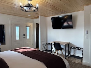Ein Hotelzimmer mit Bett, Schreibtisch, Stuhl, Fernseher und Deckenventilator.