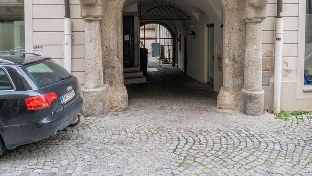 A building with a stone archway entrance, numbered 11 and 13, leading to a cobblestone street.