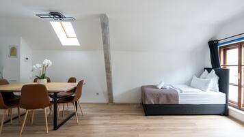 A modern room with a wooden dining table, chairs, a bed with a headboard, and a skylight.