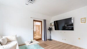 A modern living room with a sofa, a small table, a TV, and a sliding door leading to another room.
