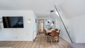 A modern apartment with a dining area, a TV mounted on the wall, and a staircase leading to an upper level.