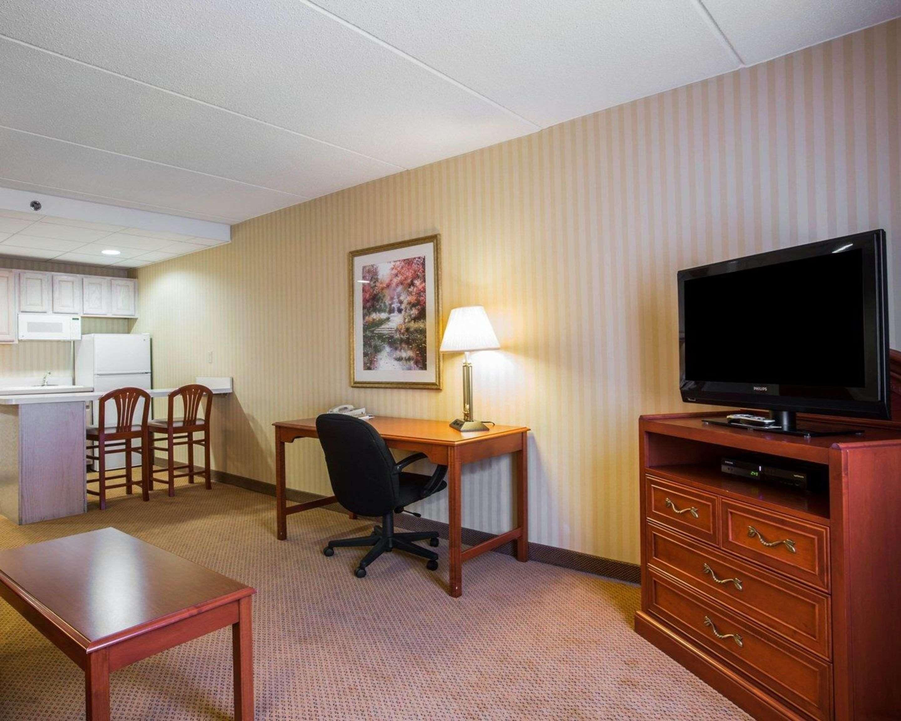 A hotel room with a kitchenette, a desk with a chair, a television, and a lamp.
