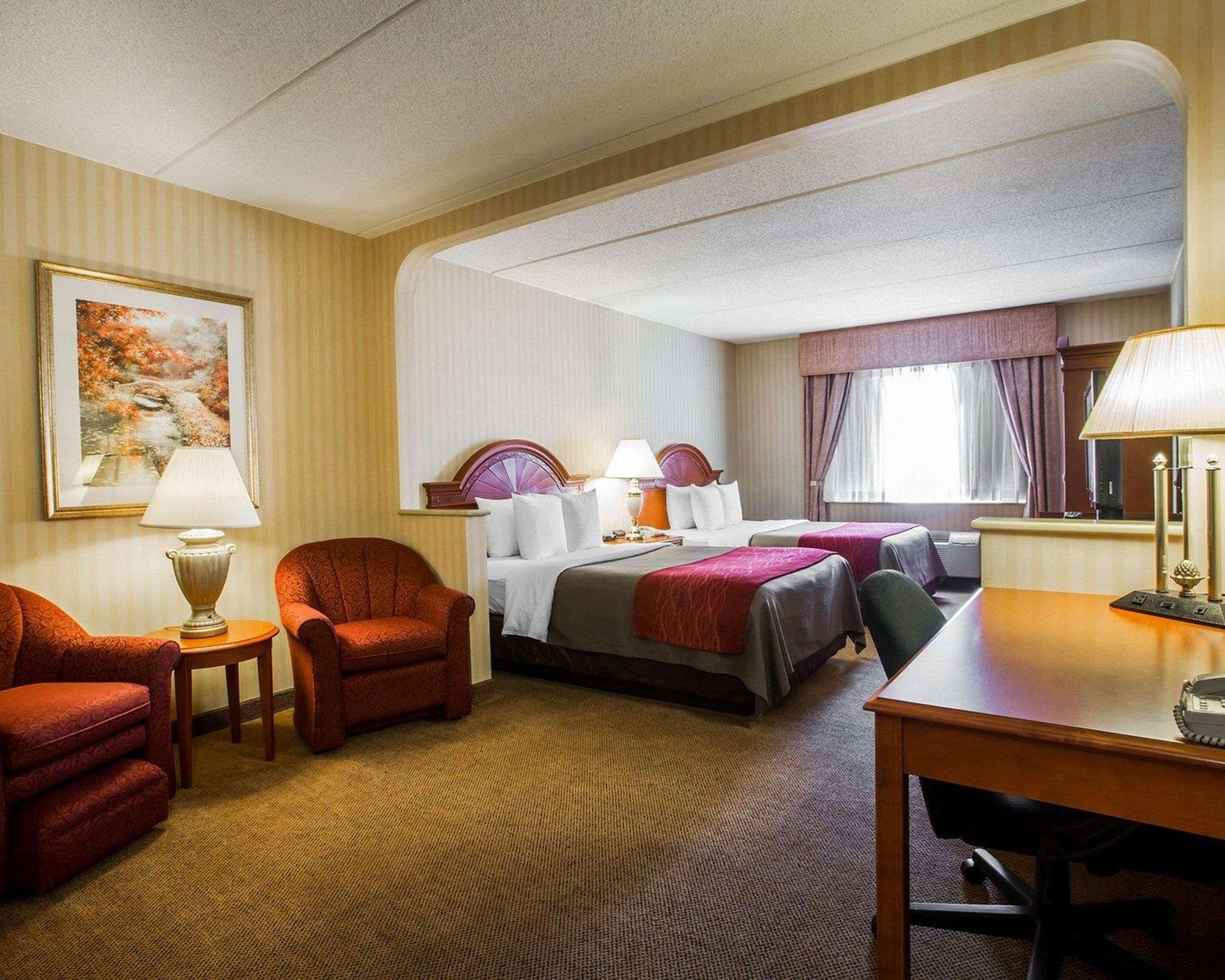 A hotel room with a large bed, two bedside tables with lamps, a chair, a desk, and a painting on the wall.