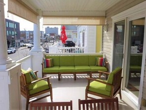 Ein überdachter Balkon mit einem grünen Sofa, Holzstühlen und Blick auf die Straße.