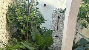 Dos sillones con cojines, una pequeña mesa de madera y abundante vegetación en un patio.