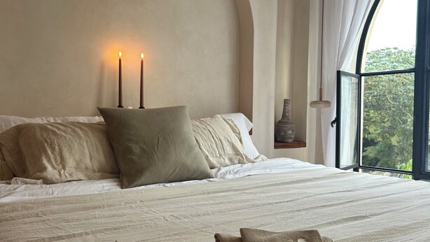 Un dormitorio con una cama grande, dos velas, una mesita de noche y una ventana con cortinas.