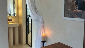 Una habitación con un escritorio de madera, una vela encendida, un espejo y una cortina blanca.