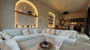 Una sala moderna con un sofá seccional, una mesa de centro redonda y estanterías empotradas con libros y objetos decorativos.