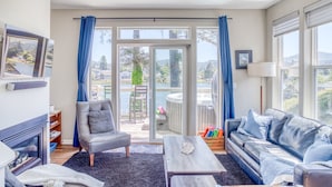 Un salon avec une cheminée, un canapé, une table basse et une vue sur un balcon équipé d’un jacuzzi.