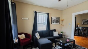 A living room with a sofa, armchair, coffee table, and a dining area with chairs. - College St. Cottage just 10 minutes from WEC. (Wilmington)