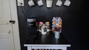 A kitchenette with a Keurig coffee maker, jars of condiments, a plant, and hanging mugs. - College St. Cottage just 10 minutes from WEC. (Wilmington)