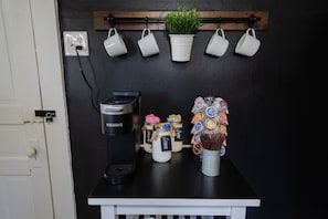 Eine Küchenzeile mit einer Keurig-Kaffeemaschine, Gewürzgläsern, einer Pflanze und aufgehängten Tassen.