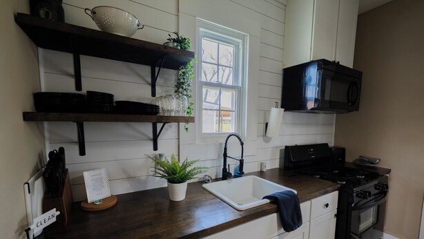 A kitchen with a dark wooden countertop, white cabinets, a black microwave, and a stove. - College St. Cottage just 10 minutes from WEC. (Wilmington)