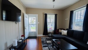 A living room with a flat-screen TV, a sofa, a coffee table, and a black rug. - College St. Cottage just 10 minutes from WEC. (Wilmington)
