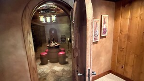 A narrow hallway with a wooden door, a stone floor, and a small table with bottles and stools.