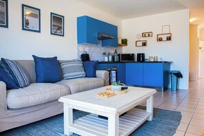 Ein modernes Wohnzimmer mit Sofa, Couchtisch und Küchenbereich mit blauen Schränken.
