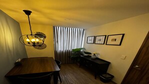 A dining area with a wooden table and chairs, a chandelier, a black console table with a vase, and a window with curtains. - Lourdes Executive Suites 201 (Bogotá)