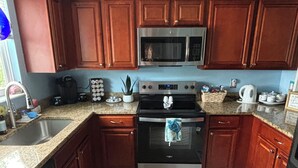 Una cocina con gabinetes de madera, un microondas, un horno, una cafetera y un hervidor.