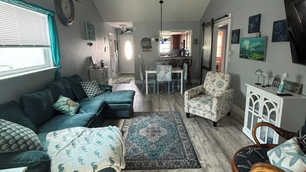 Una sala de estar con un sofá modular, un tapete estampado, un ventilador de techo y un comedor con una mesa y sillas.