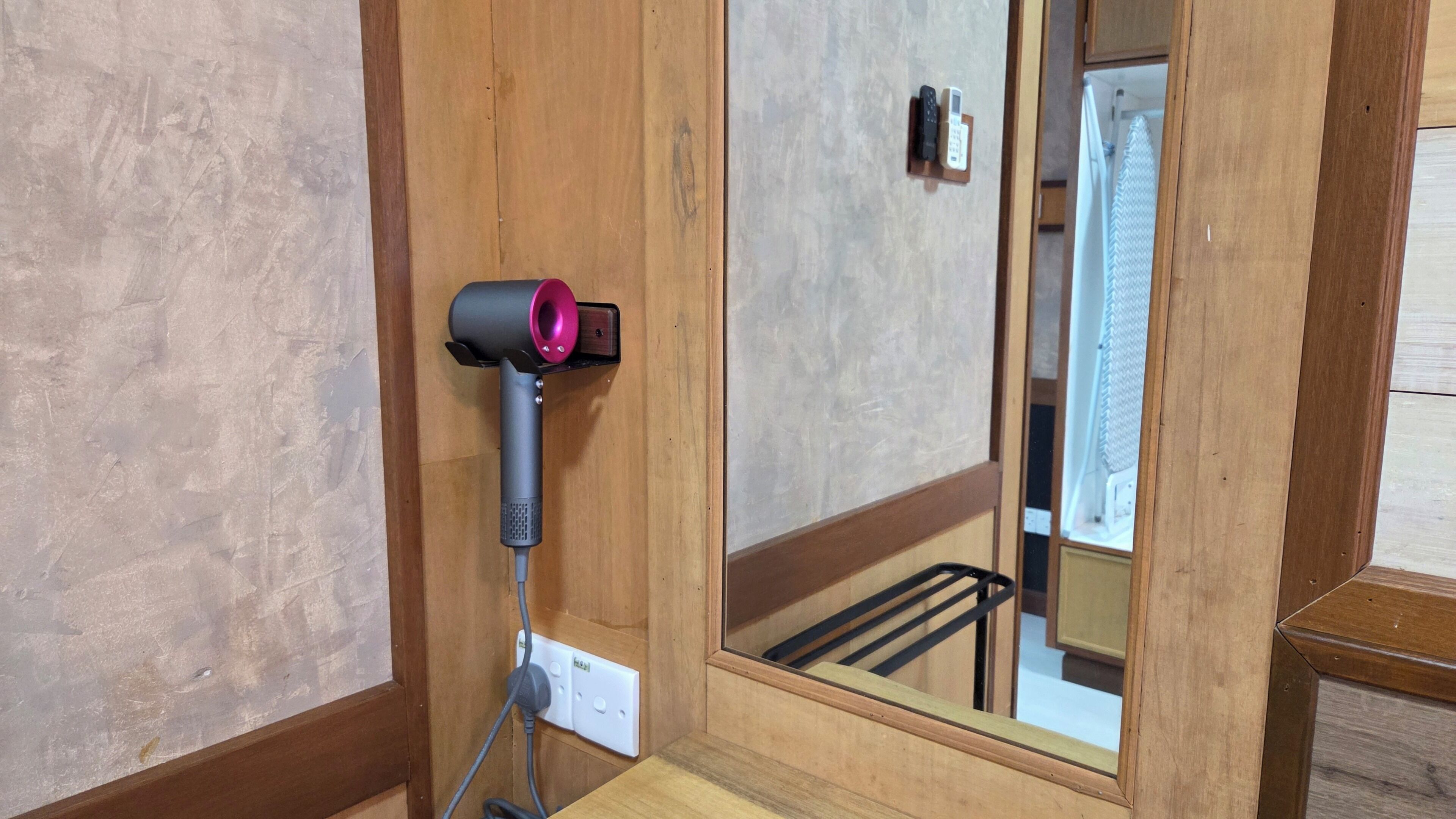 A room with a wooden door, a mirror, and a hairdryer mounted on the wall.