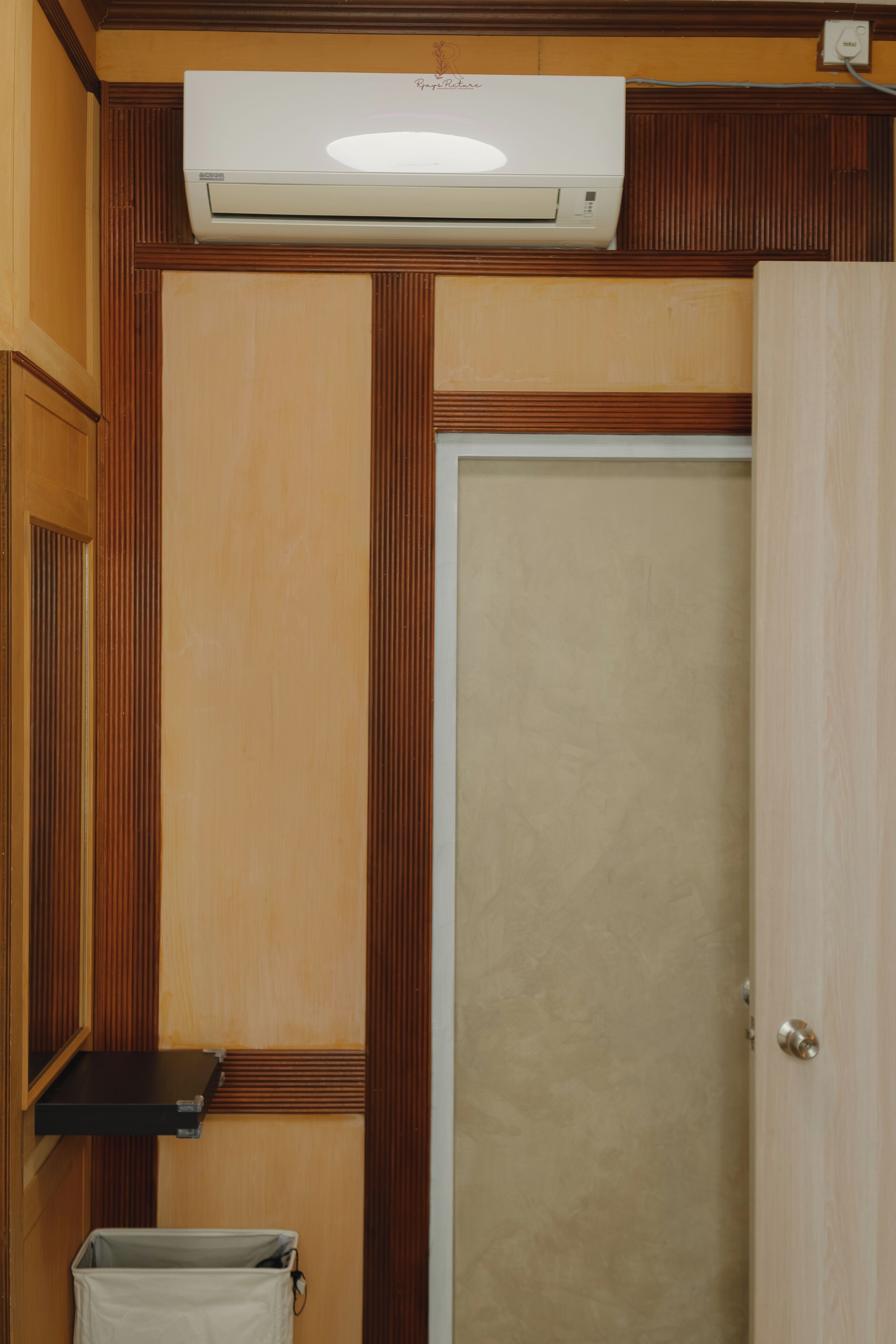 A room with a wooden panel wall, a white door, and a ceiling-mounted air conditioning unit.