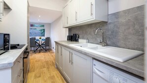 Una cocina moderna con armarios blancos, encimera gris, lavavajillas integrado y ventana con vistas a árboles.