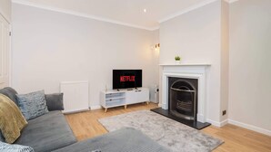 Una sala de estar con sofá, chimenea, televisor y radiador.