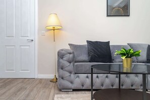 A living room with a grey sofa, a floor lamp, a round coffee table, and a potted plant.