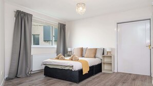 A bedroom with a bed, a radiator, a window with curtains, a door, and a chandelier. - Parking Aberdeenshire Retreat Central Peterhead (Aberdeenshire)