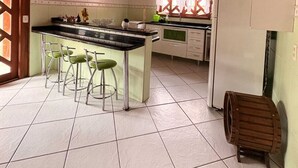 Een keuken met een houten plafond, een centraal eiland met barstoelen, een koelkast en een raam met gordijnen.