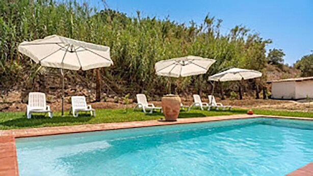 Una piscina con sillones de descanso y sombrillas.