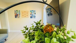 A potted plant hanging from a ceiling fixture in a room with a light-colored floor, a sofa, and wall art.