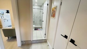 A hallway leading to a bathroom with a shower, a toilet, and a sink.