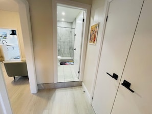 Een gang die leidt naar een badkamer met een douche, toilet en wastafel.